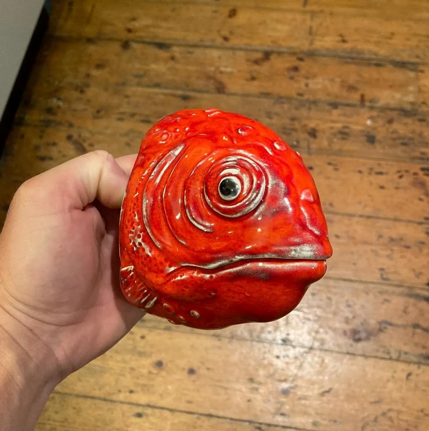 Handmade ceramic Fish wall sculpture held in a hand, showing its cognac red glaze.